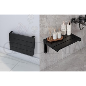 May include: Black, wall-mounted shower bench with a slatted design. The bench is folded up against the wall in one image and extended in another. The bench is made of wood and has a modern design. The bench is shown in a bathroom setting.