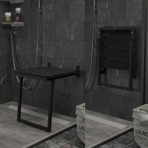 May include: Black folding shower seat with a wooden seat and metal frame mounted to a tiled wall. The seat is folded up and is in a bathroom setting.