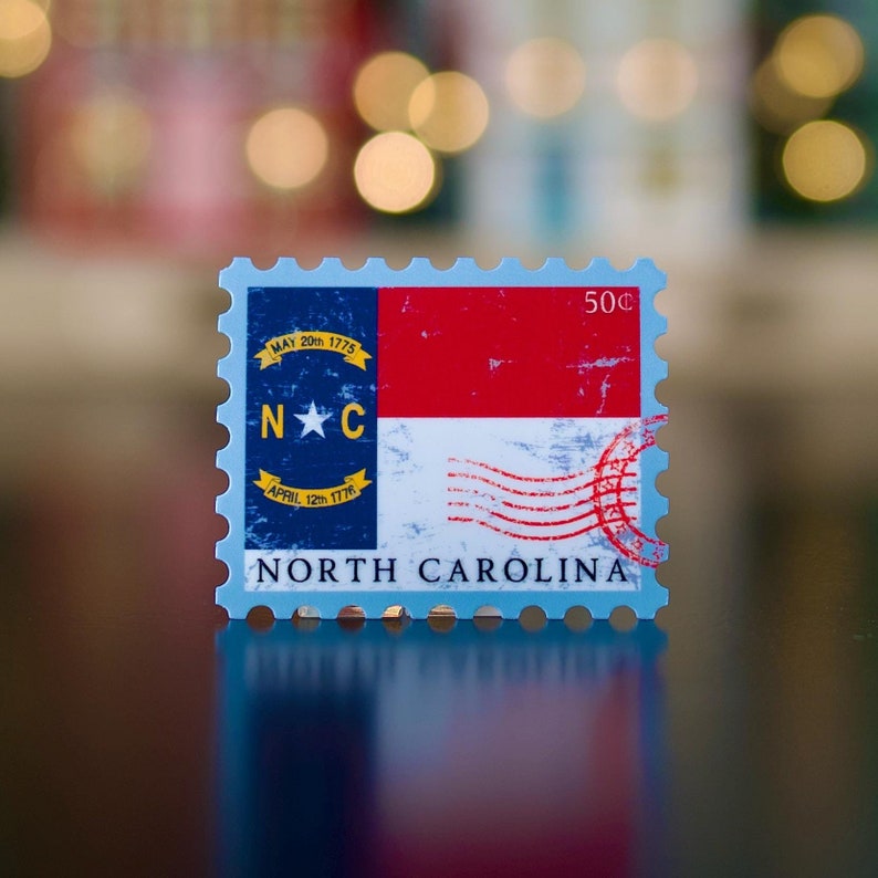 May include: A blue and white postage stamp featuring the North Carolina state flag. The stamp includes the text "MAY 20th 1775", "APRIL 12th 1776", "N.C." and "NORTH CAROLINA". The stamp also displays "50c" in the top right corner.