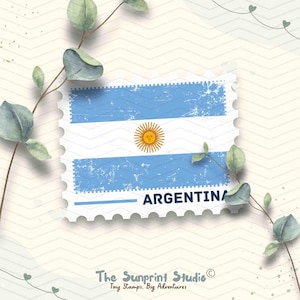 May include: A postage stamp design featuring the Argentinian flag, with light blue stripes and a central sun emblem. The word "ARGENTINA" is printed below the flag. The stamp is surrounded by a decorative border and sprigs of greenery.