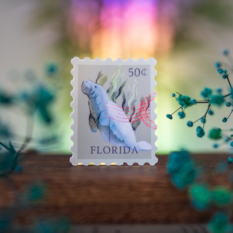 May include: A vintage-style Florida postage stamp featuring a watercolor illustration of a manatee swimming in a bed of seaweed. The stamp is labeled "50&cent;" and "FLORIDA".