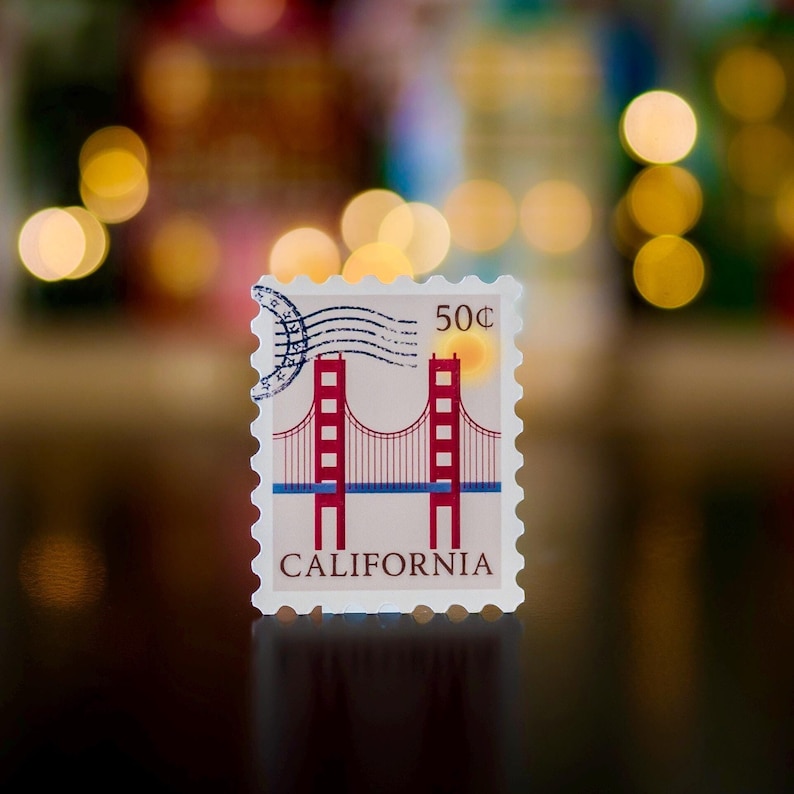 Pode incluir: Um selo postal vermelho, branco e azul com uma imagem da Ponte Golden Gate em S&atilde;o Francisco, Calif&oacute;rnia. O selo diz "50c" e "CALIFORNIA".