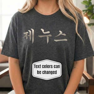 Może przedstawiać: Ciemnoszara koszulka z koreańskim tekstem w kolorze srebrnym. Poniżej tekstu znajduje się czarno-białe pole tekstowe z napisem "Text colors can be changed". Koszulka jest noszona przez osobę.