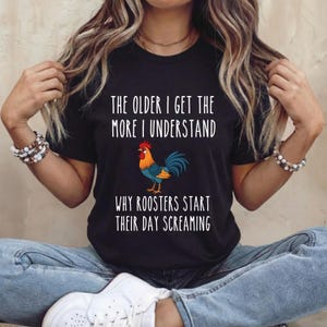 May include: Black t-shirt with the text "THE OLDER I GET THE MORE I UNDERSTAND WHY ROOSTERS START THEIR DAY SCREAMING" and a cartoon rooster illustration. The rooster is orange, blue, and yellow.