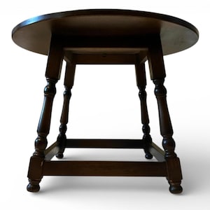 May include: A dark brown, round wooden table with four turned legs. The table has a classic design, with a circular tabletop and a sturdy base. The legs are connected by horizontal supports, providing stability. The table is suitable for various uses.