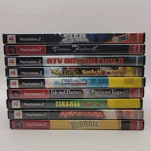 May include: A stack of ten PlayStation 2 video game cases. The games include: Sled Storm, Virtua Fighter 4, ATV Offroad Fury 2, Shrek Smash & Crash Racing, Splashdown Rides Gone Wild, Jak and Daxter: The Precursor Legacy, Pinball Hall of Fame, Defender, and Thrillville.