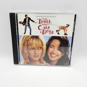 May include: A CD case for "The Truth About Cats & Dogs" soundtrack. The cover shows a man with flowers, a dog, and two women. The title is in a decorative font, with the words "Cats & Dogs" in a playful style.
