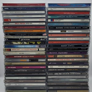Puede incluir: Una pila de discos compactos (CD) con varios artistas y títulos de álbumes. Los CD están dispuestos verticalmente, con las espinas hacia el espectador. Algunos de los títulos incluyen "Real McCoy", "OperaBabes", "Dolly Parton Super Hits", "Garth Brooks Scarecrow", "The Digital Age", "Tripping Daisy", "Switchfoot", "How Great Is Our God", "Lifescapes", "St. Germain", "702", "Frank Sinatra", "The Wannadies", "Carbon Leaf", "Luciano Pavarotti", "Barbra Streisand Duets", "Travis", "Alabama Dancin' On The Boulevard", "Buddy Jewell", "Ray Lynch", "Lucero", "Mendelssohn/Beethoven-Stern", "TLC Creep", "Mindless Self Indulgence", "George Strait", "Take 6", "Kenny G", "Frank Sinatra".
