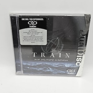 Könnte beinhalten: Ein schwarzes und silbernes CD- und DVD-Kombi-Disc-Gehäuse mit einem dunkelblauen und weißen Bild eines stürmischen Meeres. Das Gehäuse trägt den Text "TRAIN MY PRIVATE NATION" und das Logo "DualDisc".