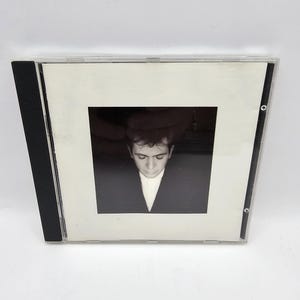 May include: A black and white photo of a man in a suit, looking down. The photo is on a white background and is in a clear plastic CD case.