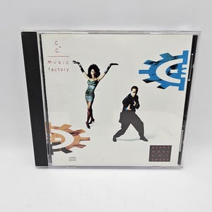 May include: A CD cover with a white background featuring a man and a woman in front of a large blue gear with the letter C in the center. The text "C+C music factory" is in the top left corner and the text "gonna make you sweat" is in the bottom right corner.