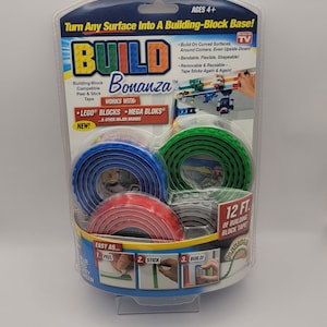 May include: A package of Build Bonanza building block tape. The tape is compatible with LEGO® and MEGA BLOKS® building blocks. The package shows the tape in blue, red, green, and gray. The tape is 12 feet long and can be used to build on curved surfaces, around corners, and even upside down. The tape is bendable, flexible, and shapeable. It is also removable and reusable. The tape sticks again and again.