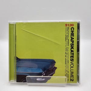 May include: A CD case with a green background and a blue car on the front. The text on the case reads "CHEAPSKATESVOLUME2" and "BEC RECORDINGS PRESENTS THE OC SUPERTONES CADET PLANKEYE ANY GIVEN DAY: EARTH TO HEAVEN HANGNAIL FLIGHT 180 ACE TROUBLESHOOTER JOY ELECT HARMONICS ULTRABEAT HIP HOP PRAISE MG THE VISIONARY THE COMPANY LOS DOGS".