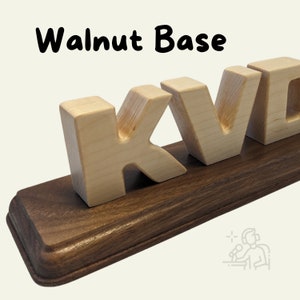 This image showcases a Walnut Base with a smooth, rich brown finish and rounded edges. It holds light wooden block letters, creating a contrast between the dark base and the natural wood tone of the letters.