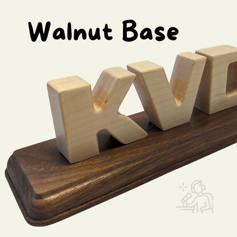 This image showcases a Walnut Base with a smooth, rich brown finish and rounded edges. It holds light wooden block letters, creating a contrast between the dark base and the natural wood tone of the letters.