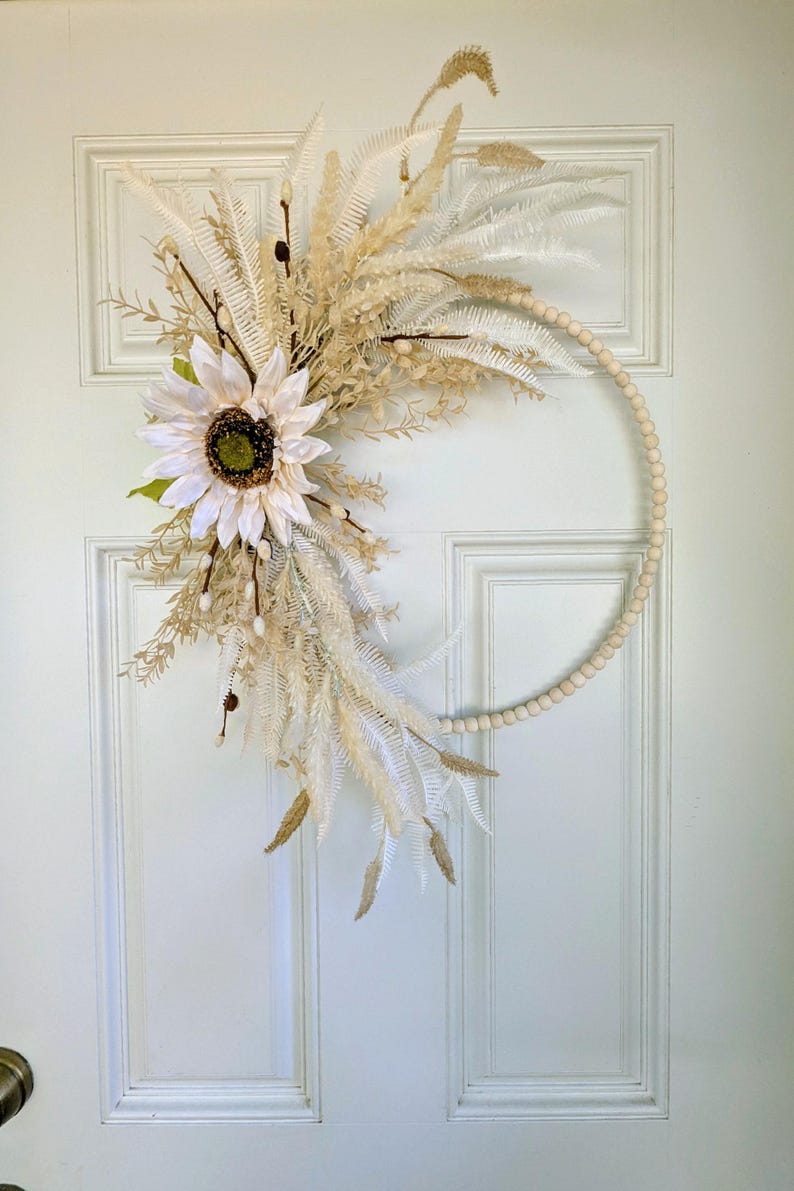 May include: A white sunflower and dried pampas grass wreath with a natural wood bead base.