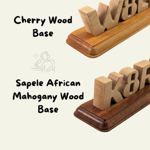 This image compares two wooden bases. The top is a Cherry Wood Base with a light, warm tone. The bottom is a Sapele African Mahogany Wood Base, darker with a richer reddish-brown hue. Both feature smooth, rounded edges, holding block letters.