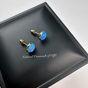 May include: A pair of opal stud earrings with gold settings. The earrings are displayed on a black tray with the text "Natural Diamonds of NYC".
