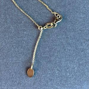 Puede incluir: Un collar de cadena de oro con un pequeño dije redondo y un cierre de langosta. El cierre tiene la inscripción "18kt Italy".