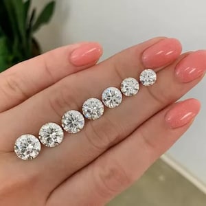 May include: A collection of seven round-cut diamonds of varying sizes, arranged in a diagonal line. The diamonds are clear and sparkling, reflecting light. The diamonds are displayed on a light skin tone.