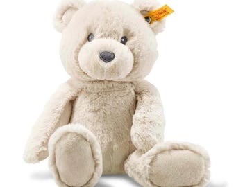 Puede incluir: Un oso de peluche con pelaje suave de color crema, ojos redondos oscuros y una nariz gris oscuro bordada. El oso está en posición sentada y tiene una pequeña etiqueta amarilla unida a la oreja derecha con el texto Steiff Knopf im Ohr.