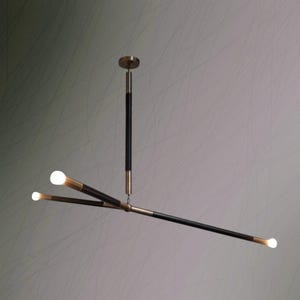 May include: Modern chandelier with a black and brass finish. The light fixture has three arms with integrated LED bulbs. The central stem is black with brass accents, and the bulbs emit a warm, white light. The design is minimalist and contemporary.