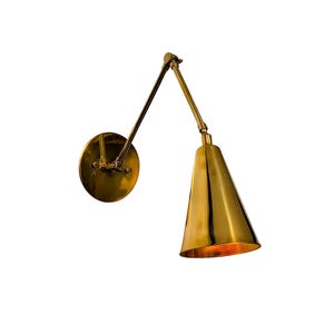 Könnte beinhalten: Eine Wandleuchte aus poliertem Messing mit einer runden Montageplatte, einem verstellbaren, zweiteiligen Gelenkarm mit sichtbaren Verbindungen und einem nach unten gerichteten konischen Schirm. Die metallische Oberfläche reflektiert das Licht.