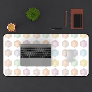 Può includere: Un tappetino da scrivania rettangolare bianco con un motivo ripetuto di forme geometriche colorate. Un laptop, un mouse, una tazza di caffè, un taccuino, una penna e una piccola pianta sono disposti su una superficie scura.