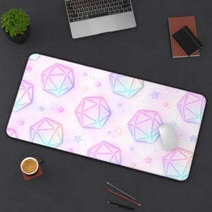 May include: A rectangular mousepad with a pastel pink background featuring geometric shapes in shades of blue, purple, and green. The design includes small star shapes. A white mouse rests on the pad, next to a laptop.