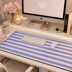 May include: A rectangular desk mat featuring a repeating pattern of horizontal light blue and white stripes with a black border. The mat is positioned on a white desk surface, providing a flat, smooth area for a white computer keyboard and mouse.
