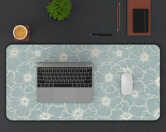 Puede incluir: Una alfombrilla de escritorio azul claro con un patrón floral blanco. Un ordenador portátil, un ratón inalámbrico y una taza de café están sobre la alfombrilla de escritorio.