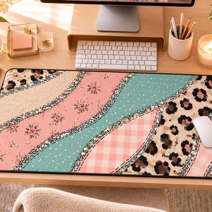 Könnte beinhalten: Eine rechteckige Schreibtischunterlage mit einem Patchwork-Design aus wellenförmigen Abschnitten. Die Muster umfassen florale Drucke in Rosa, Türkis mit weißen Punkten, hellrosa Vichy-Karo und Leopardenmuster, getrennt durch glitzernde Ränder.