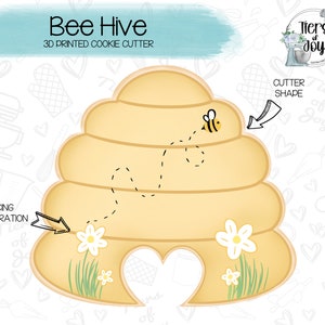 May include: A 3D printed cookie cutter shaped like a beehive with a bee flying around it. The cutter is yellow and has a heart-shaped opening at the bottom. The image also includes the text "Bee Hive" and "3D Printed Cookie Cutter".
