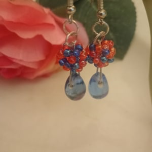 Puede incluir: Un par de pendientes colgantes con racimos de cuentas azules y naranjas y cuentas de vidrio azul en forma de lágrima.