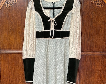 Puede incluir: Un vestido largo blanco maxi con estampado floral y mangas de encaje. El vestido tiene un corpiño de terciopelo verde con ribete de encaje y un lazo en el escote.
