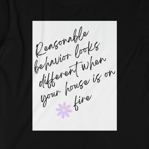May include: Black t-shirt with a white rectangle. The text reads "Reasonable behaviour looks different when your house is on fire" in a handwritten font. A small purple flower is below the text.