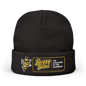 Puede incluir: Gorro negro con un gráfico amarillo y blanco de una abeja con gafas de sol y las palabras "Buzzy Bites" y "The Evolution of the Sandwich" en un rectángulo amarillo.