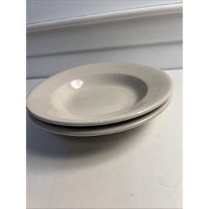 May include: Two off-white, shallow soup or pasta bowls stacked on top of each other. The bowls have a simple, classic design with a slightly raised rim. The bowls are made of ceramic or porcelain and are suitable for everyday use.