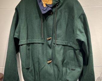 Puede incluir: Chaqueta verde oscuro con cuello alto y cierres de palanca de madera. La chaqueta tiene un forro de cuello azul y un interior acolchado dorado. La chaqueta tiene dos bolsillos delanteros y un cordón en el cuello.