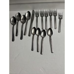 Peut inclure: Un ensemble de couverts, comprenant des cuillères et des fourchettes, tous en acier inoxydable. Les couverts sont disposés en rangée sur une surface blanche.