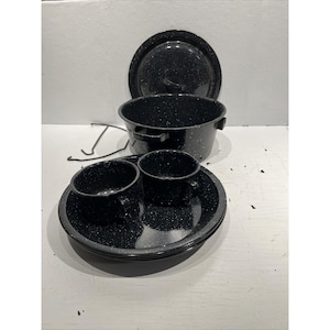 May include: A black speckled enamelware camping cookware set. The set includes a pot with a lid, two cups, and plates. The cookware is black with white speckles. The set is designed for outdoor use.