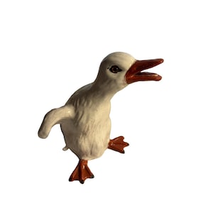 May include: A ceramic duck figurine featuring a white body with a fine crackle glaze finish. The duck has an open beak, orange webbed feet, and orange bill details. The figure is depicted in a standing position with one wing slightly extended.