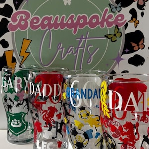 May include: Four clear pint glasses with custom designs. Each glass features a name and team-related graphics in various colors, including green, red, blue, and yellow. The background includes a logo with the text "Beauspoke Crafts" and decorative butterflies.