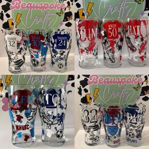 May include: Clear glass pint glasses with football-themed designs. Each glass features a team jersey design with a name and number. Some glasses have the text "MUM", "ANDY 50", and "HATCH". The glasses are decorated with footballs and team logos.