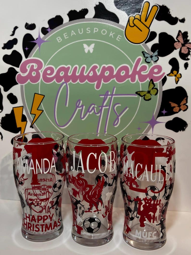 May include: Three clear pint glasses with red and black designs. Each glass has a name in white lettering. One glass says "Amanda" with "Happy Christmas" below. The other glasses say "Jacob" and "Macaule".