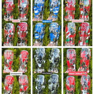 May include: A collection of clear pint glasses with various designs. Some glasses feature team names like Arsenal, Brighton, Southampton, Liverpool, Notts County, and Man United, along with names and numbers. The glasses have red, blue, and black accents.