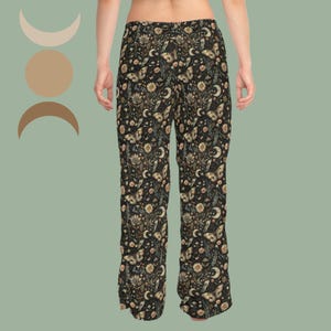 May include: Full-length trousers featuring a black background with a repeating pattern of beige and white moths, crescent moons, and various floral elements. The pants have a straight-leg cut and a fitted waistband, showcasing a detailed botanical print.