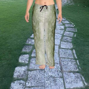 May include: Green and white patterned pajama trousers with a black drawstring. The trousers have a watercolour-like design and a relaxed fit. The model is standing on a stone path.