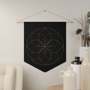 May include: A black tapestry with a gold geometric design of a flower with overlapping circles and squares. The tapestry is hanging on a white wall.
