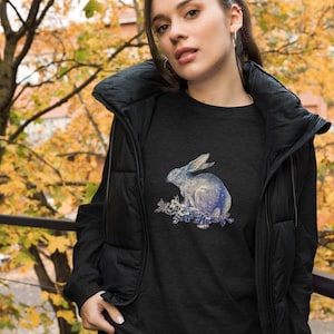 Könnte beinhalten: Ein dunkelgraues T-Shirt mit einem blauen und weißen Kaninchen-Motiv. Das Kaninchen ist von Blumen umgeben und hat ein Sternenmuster.